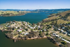 An aerial view of residential housing nestled amongst gumtrees and hills on the edge of Lake Eildon.