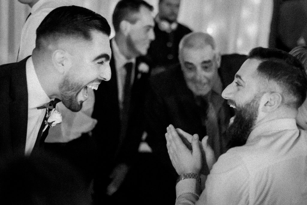 Black and White Image of a wedding party where two guests are laughing hard.